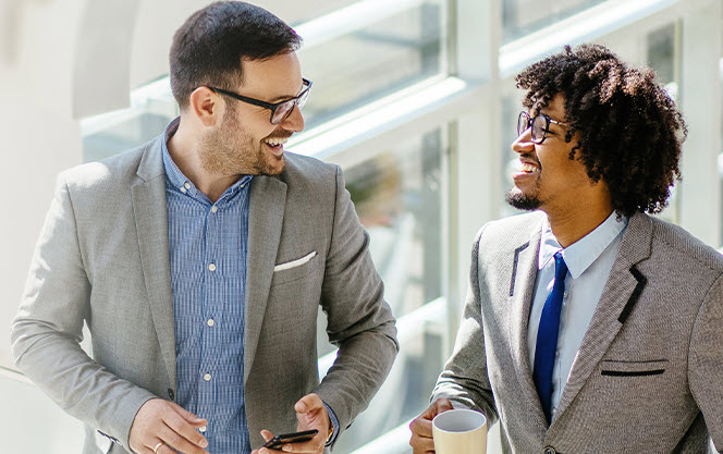 Two men in business attire smiling at each other. 